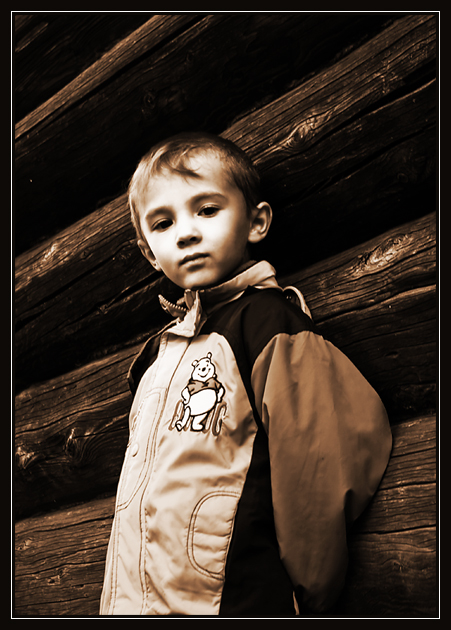портрет ребенка, стоящего у стены деревяного дома